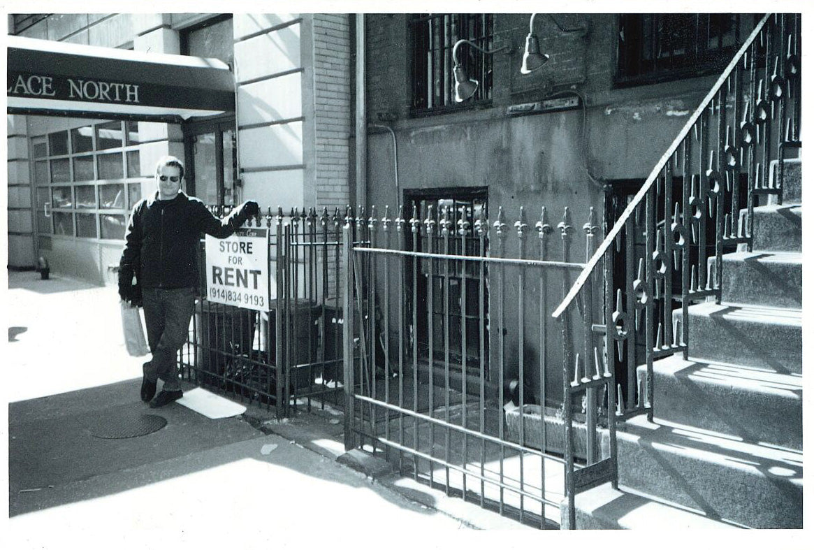 Black and white photo of a man beside a Store For Rent sign outside a Gramercy brownstone