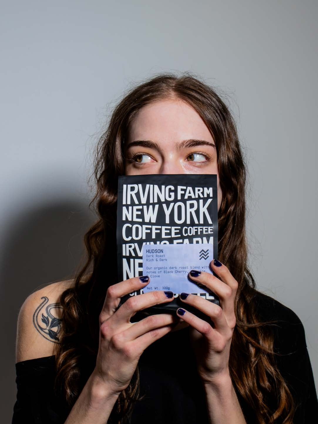A woman holding a bag of Irving Farm Hudson Dark Roast in front of her face